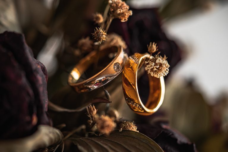 Image of two gold wedding rings hanging on a tree branch.