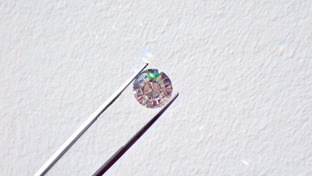 Lab gown diamonds. Image of a diamond being held with jewelry tweezers against a white background.