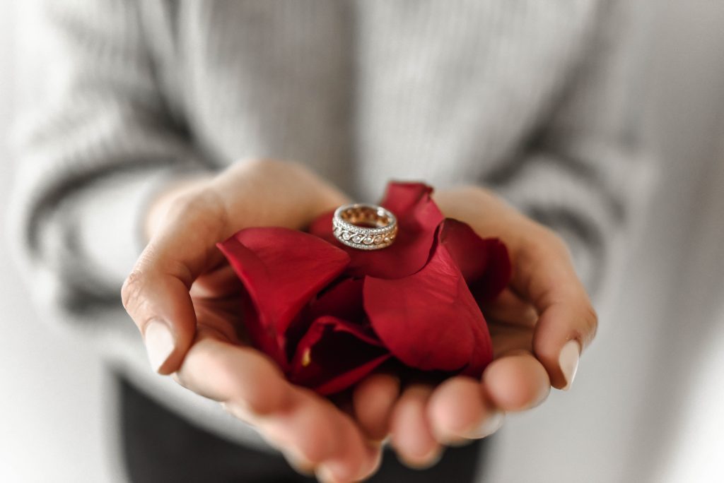 Image of a person holding a red cloth and a diamond ring jewelry sitting on it. Valentine's Day.