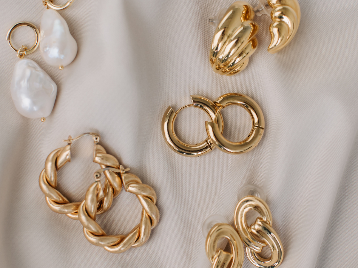 Image of gold earrings against a beige silk background. We buy jewelry, we buy gold.