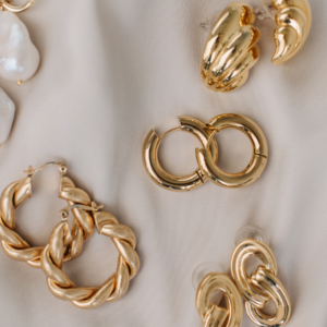 Image of gold earrings against a beige silk background. We buy jewelry, we buy gold.